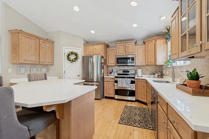 Vaulted ceilings, light wood-finish cabinetry, stainless steel appliances, white countertops, and wood-finish flooring