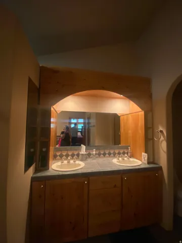 Dual vanity with wood-finish cabinetry, integrated sinks, a tiled countertop, and a tiled backsplash