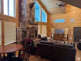 Vaulted wood-paneled ceilings with exposed beams, stone fireplace, wood-finish flooring, and expansive windows