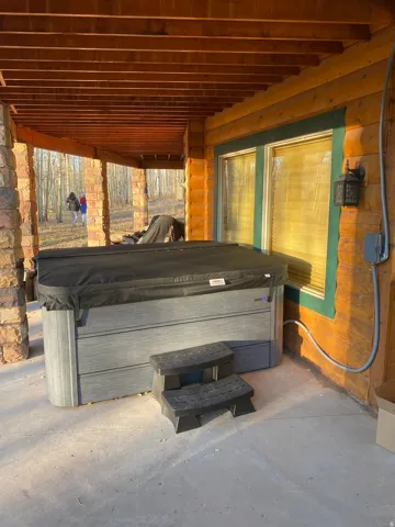 Covered outdoor patio with a built-in spa, stone columns, and wood-paneled walls
