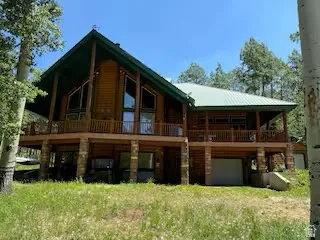 Log-sided residence featuring a prominent A-frame structure, a wide balcony, a covered porch, an attached garage, and a metal roof