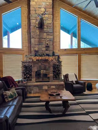 Vaulted wood-paneled ceiling, stone-clad fireplace with hearth, and large trapezoidal windows with wood trim