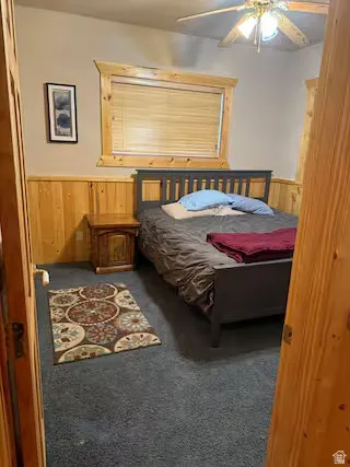 Carpeted bedroom with wood paneling, wood-trim window, and ceiling fan