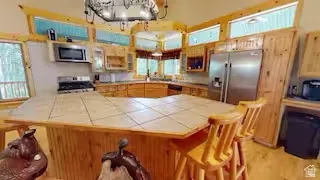 Kitchen featuring light wood cabinetry, stainless steel appliances, a tile-top island with seating, and wood-finish flooring