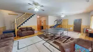 Spacious recreation room featuring wood-finish flooring, staircase with natural wood railings, and beadboard wainscoting