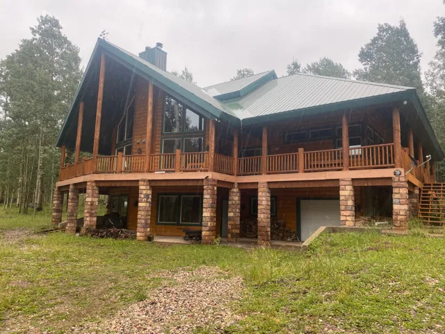 Wood-sided exterior featuring a green metal roof, expansive wrap-around deck with wood railings, and stone-clad support columns