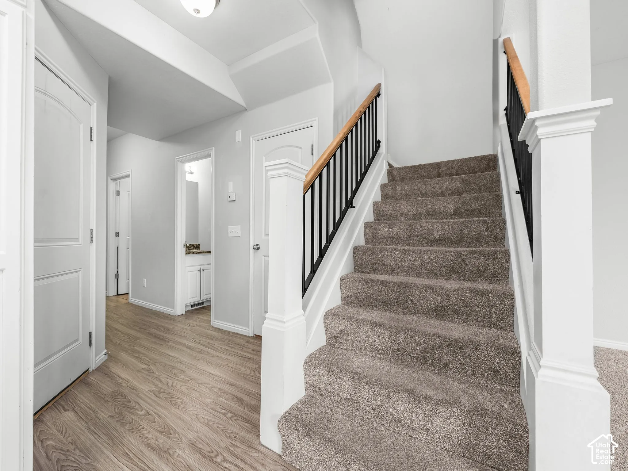 Carpeted staircase with dark iron balusters and wood-finish handrail