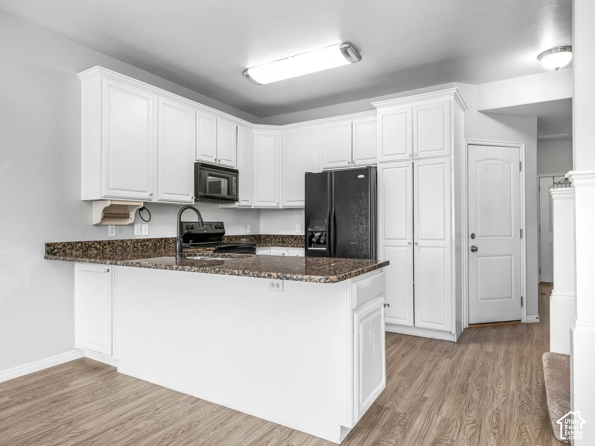 Kitchen featuring white cabinetry, wood-finish flooring, a built-in microwave, an integrated refrigerator, and a kitchen island with stone countertops