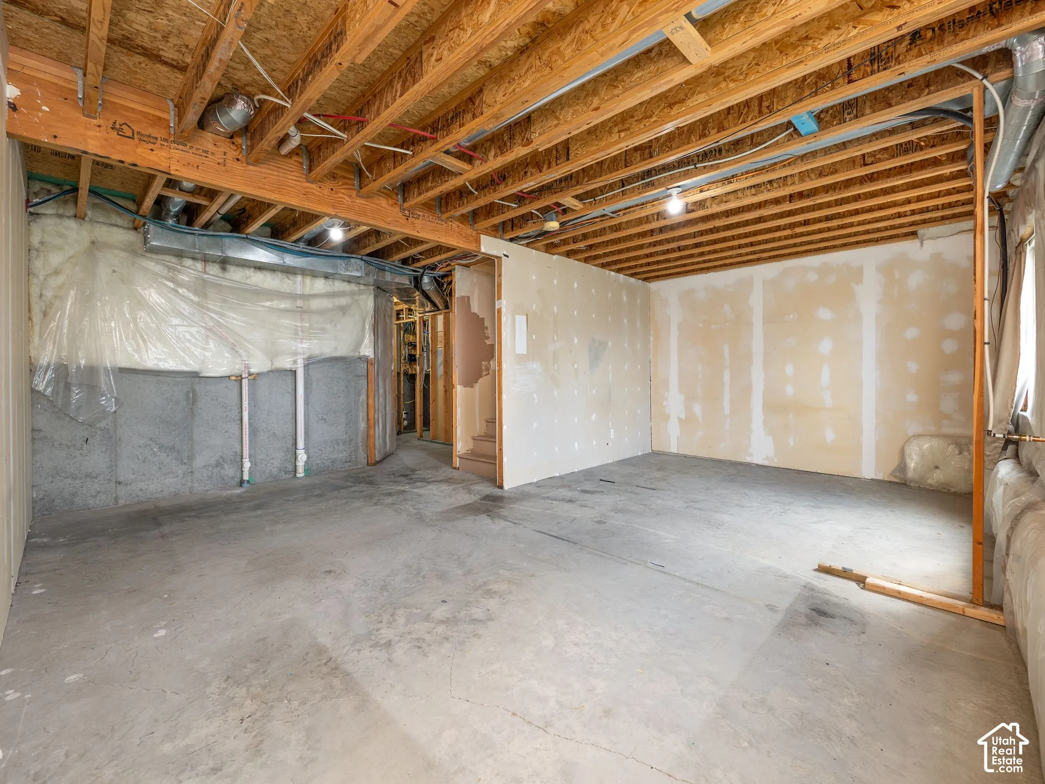 Unfinished basement with concrete flooring, exposed wood ceiling joists, and partial drywall installation