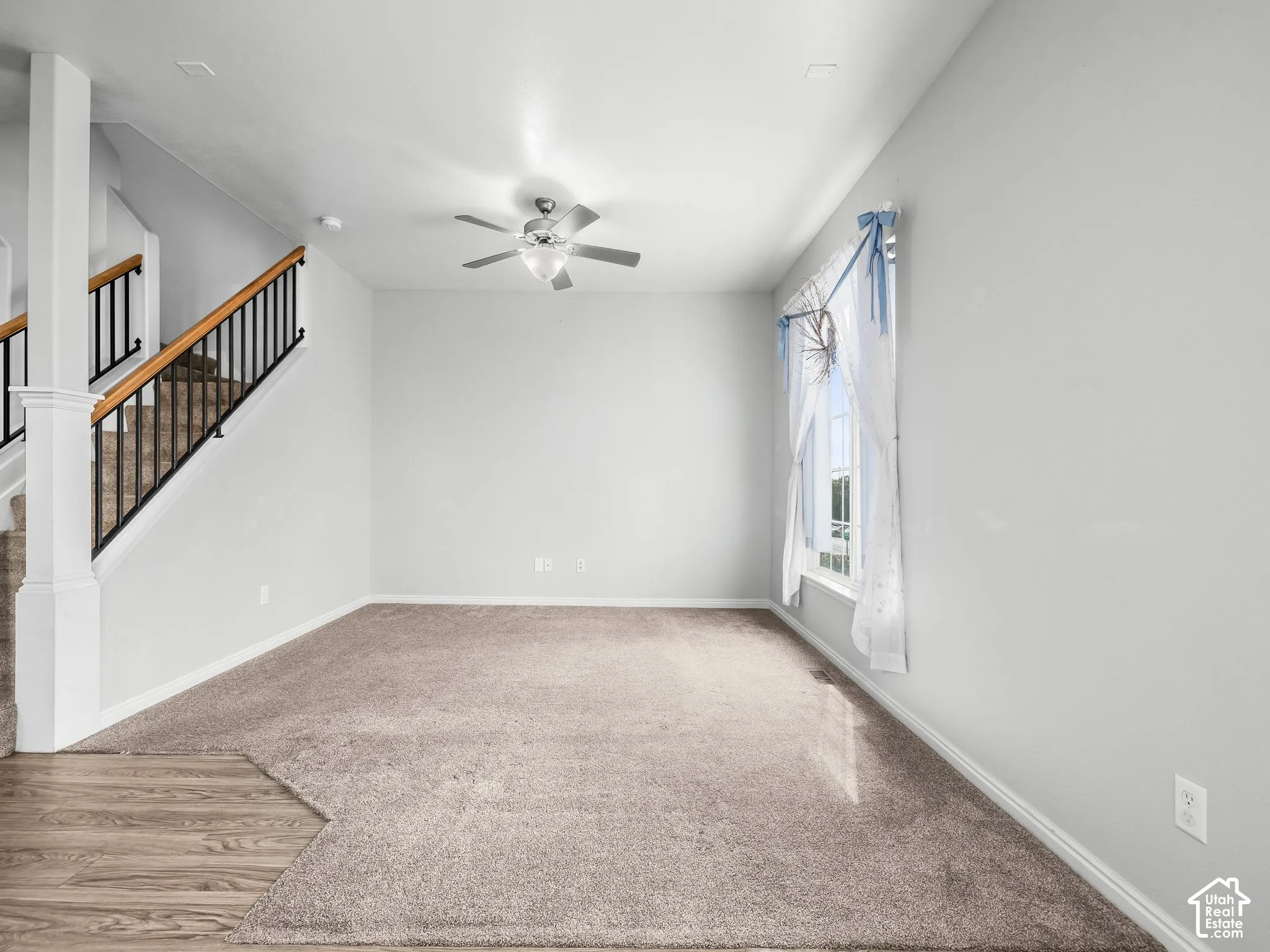 Carpeted flooring, wood-finish flooring, staircase with wood handrail and black balusters, window with trim, ceiling fan