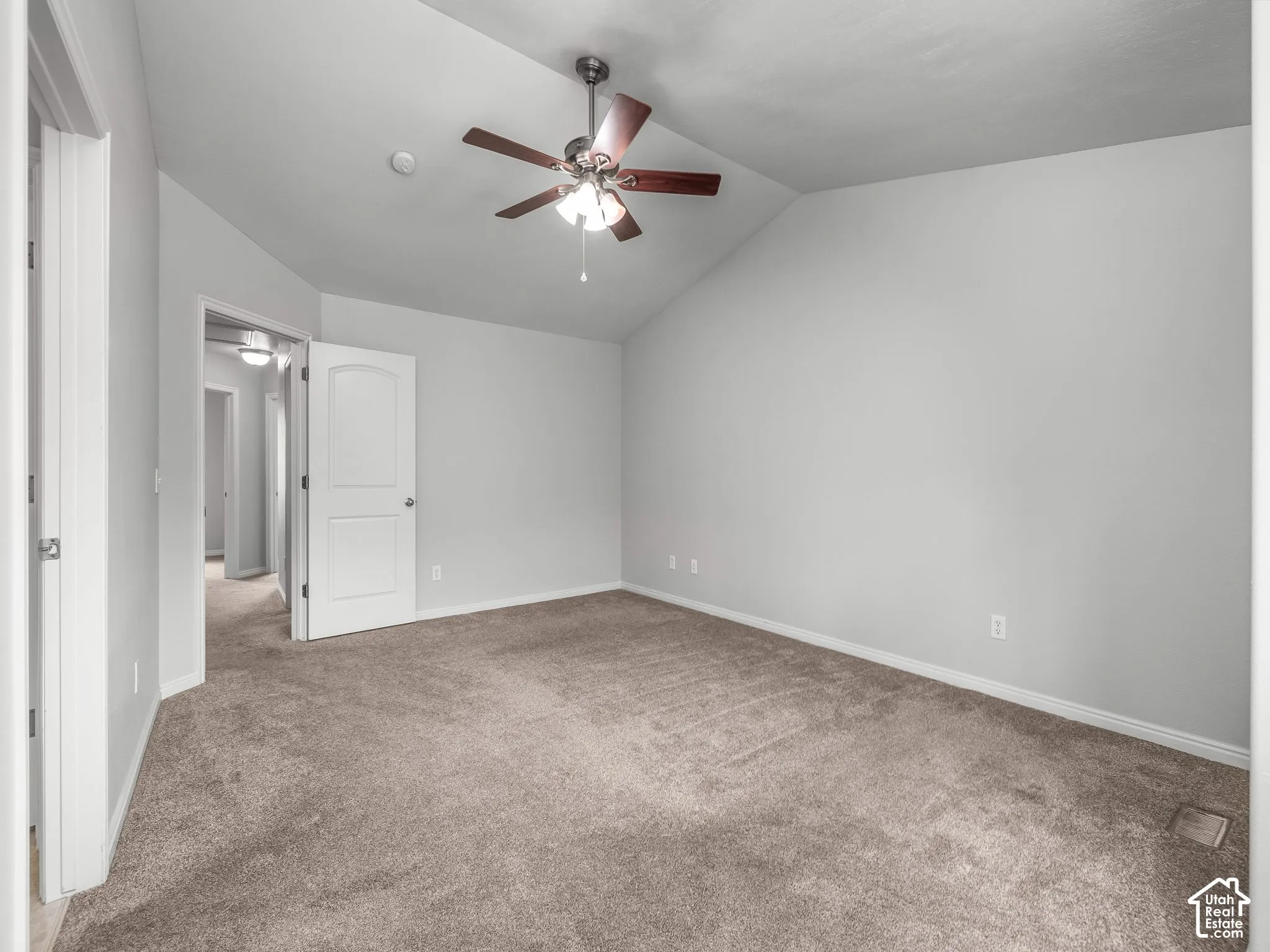 Vaulted ceiling, ceiling fan, neutral carpet, white trim, and white paneled door