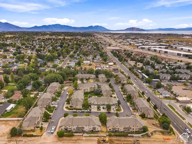 Expansive community featuring multiple residential structures with pitched roofs, surrounding mature trees, and a mountain range backdrop