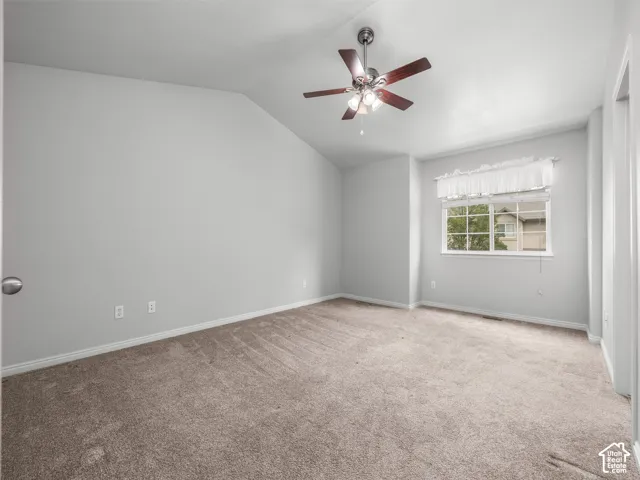 Vaulted ceiling room with neutral carpet, a single window, and a ceiling fan with integrated lighting