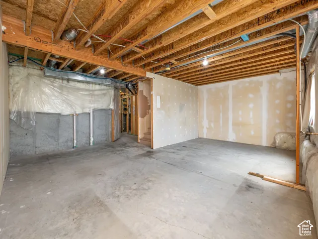 Unfinished basement with concrete flooring, exposed wood ceiling joists, and partial drywall installation