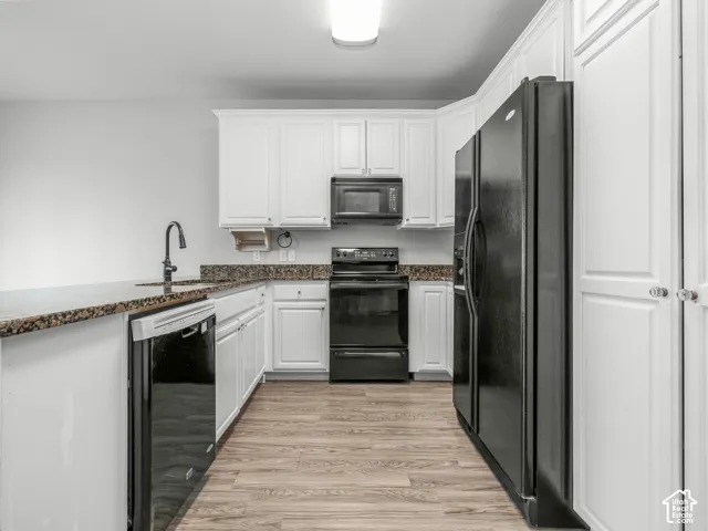 Kitchen featuring white cabinetry, dark speckled countertops, wood-finish flooring, and black appliances including a refrigerator, range, microwave, and dishwasher