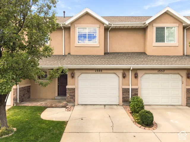 Stucco exterior with stone accents, attached garage, and pitched shingle roof