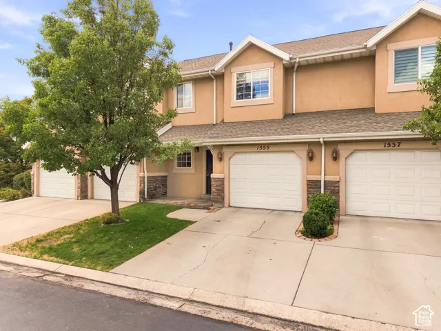 Stucco exterior with stone accents, individual garage doors, and mature landscaping