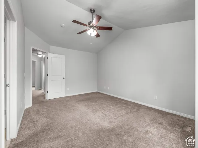 Vaulted ceiling, ceiling fan, neutral carpet, white trim, and white paneled door