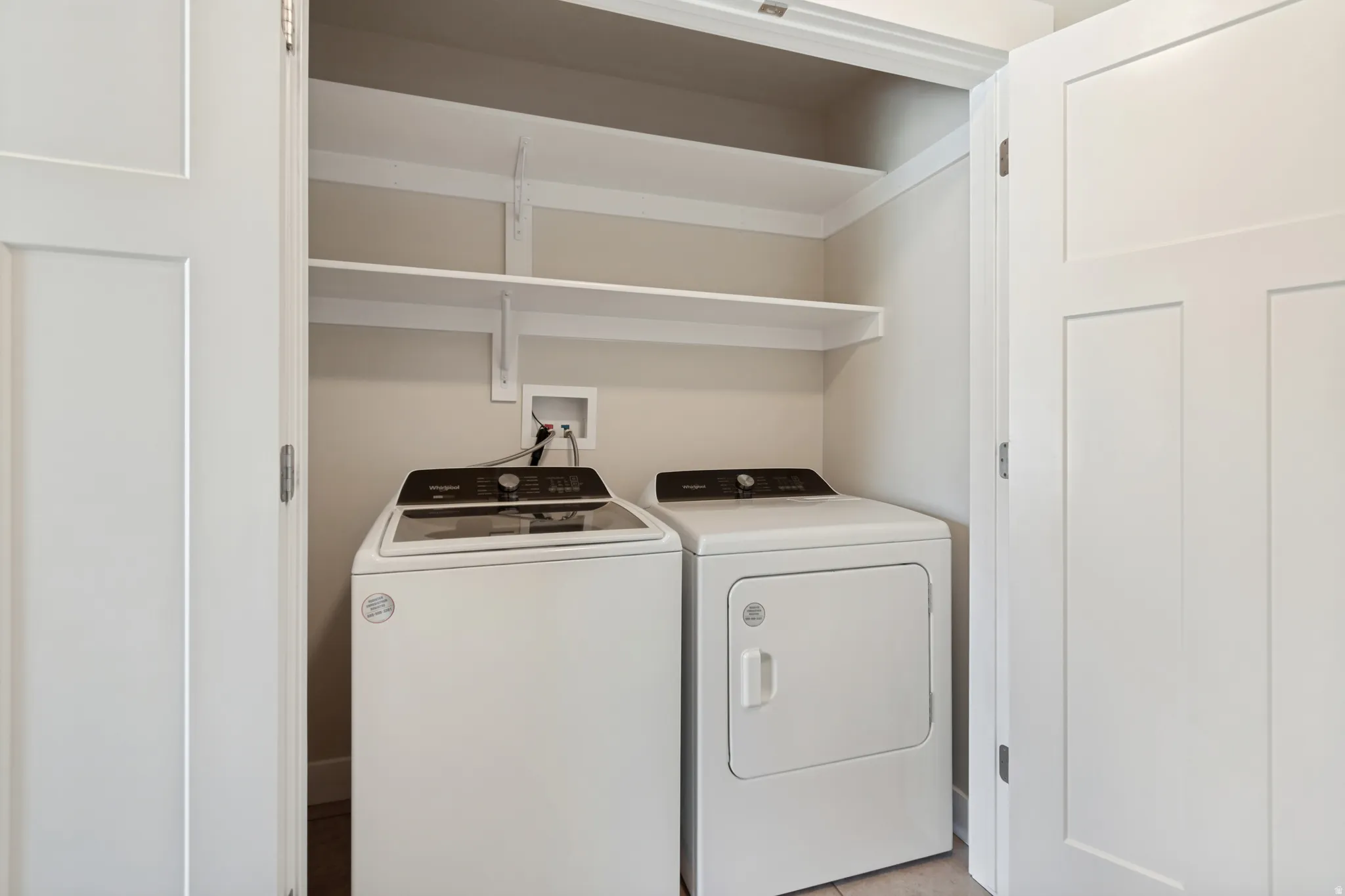 Integrated laundry area featuring white panel doors and upper shelving