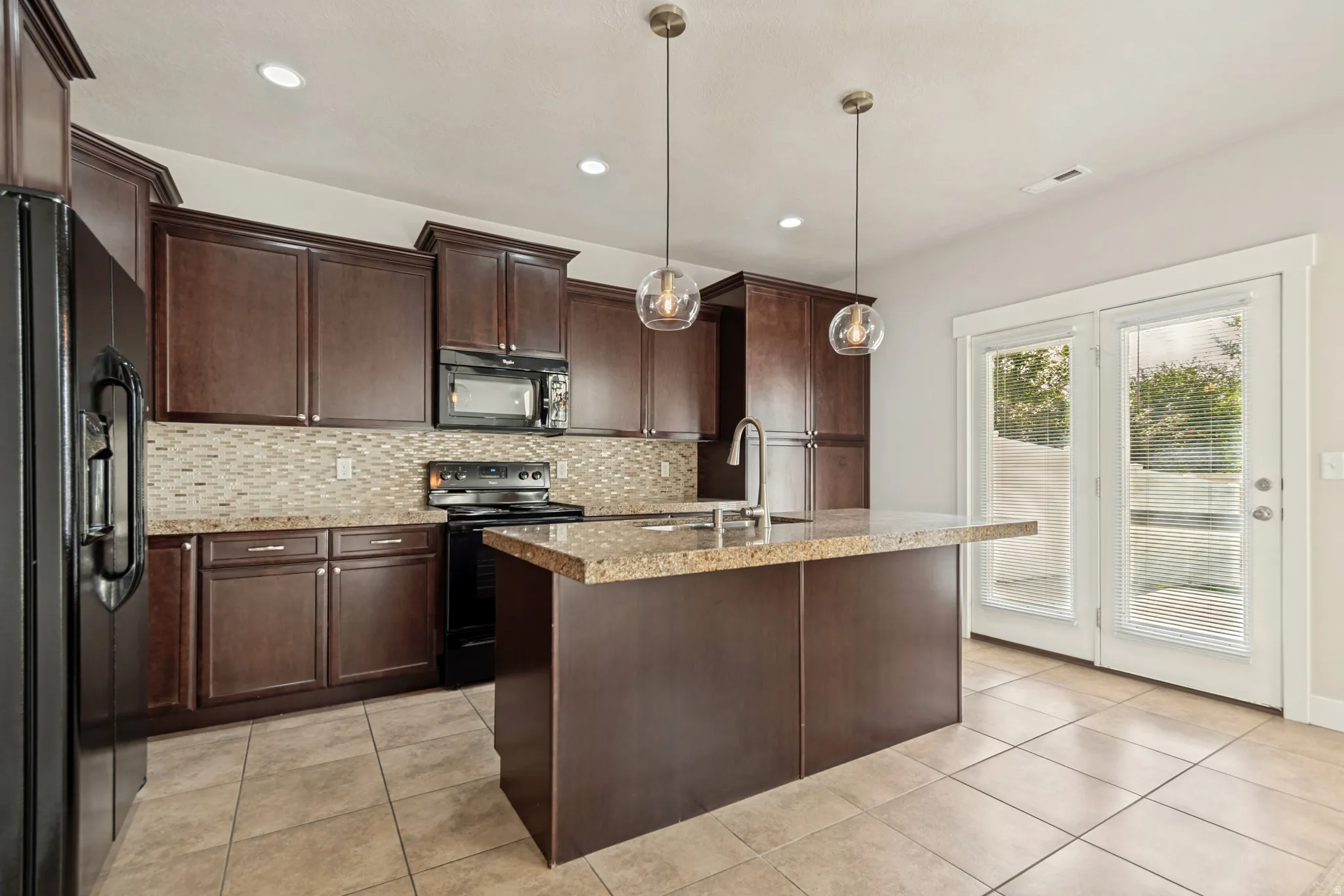 Kitchen featuring dark wood-finish cabinetry, a textured tile backsplash, a kitchen island with stone-finish countertops, and an integrated sink with a gooseneck faucet