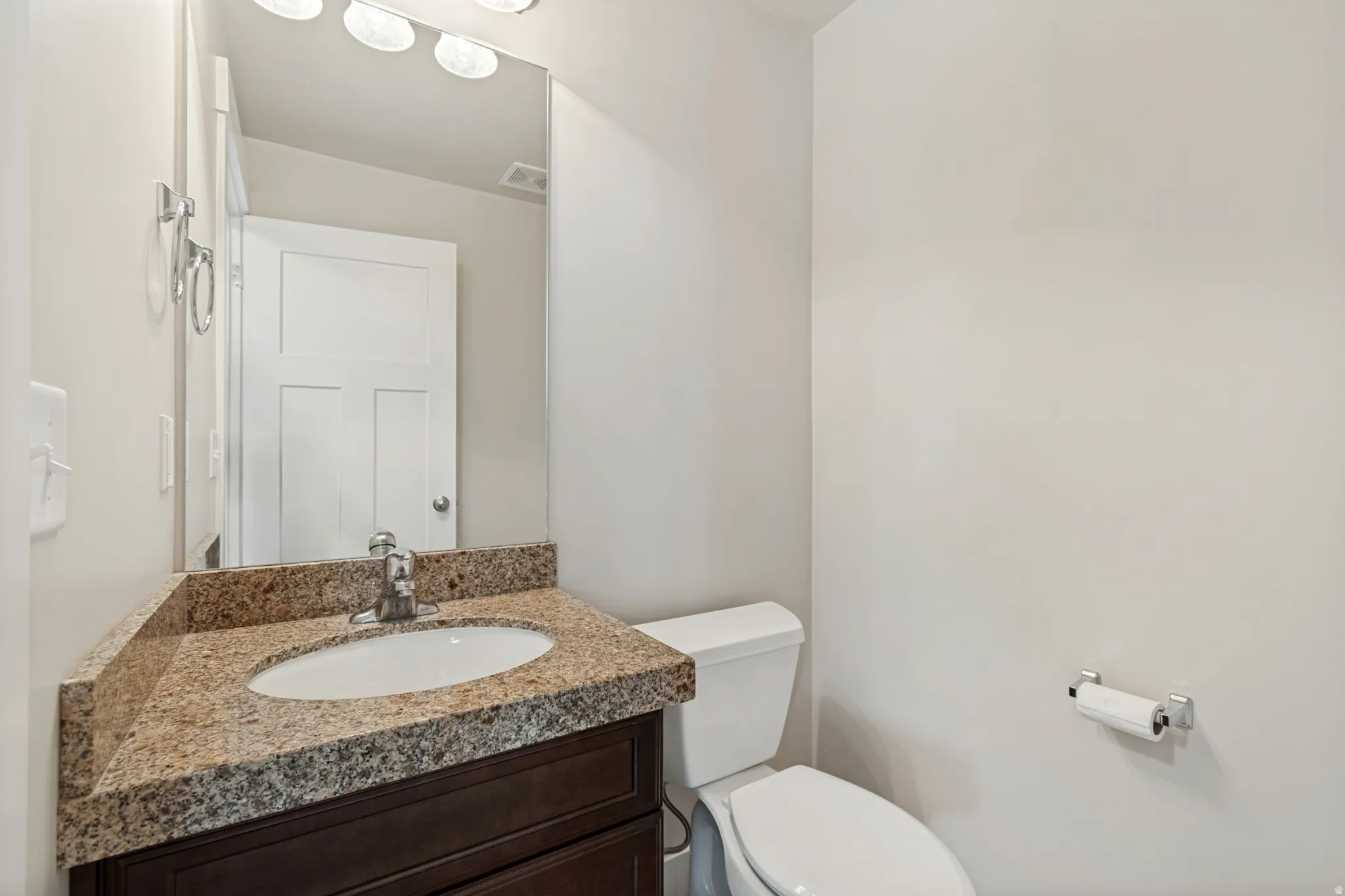 Vanity with an undermount sink, granite countertop, chrome faucet, and dark wood-finish cabinetry
