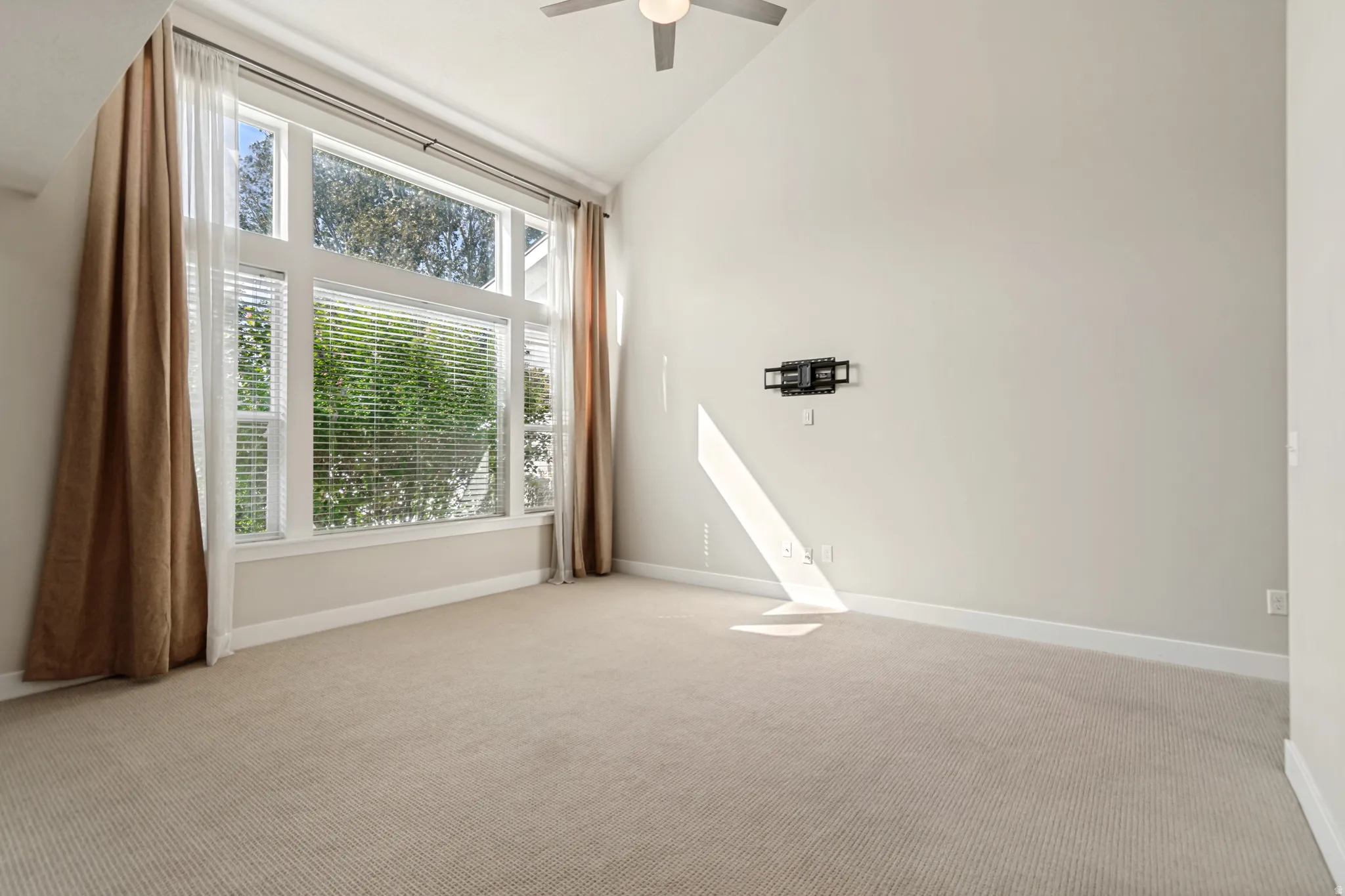 Vaulted ceilings, large windows, ceiling fan, and light-colored carpeting