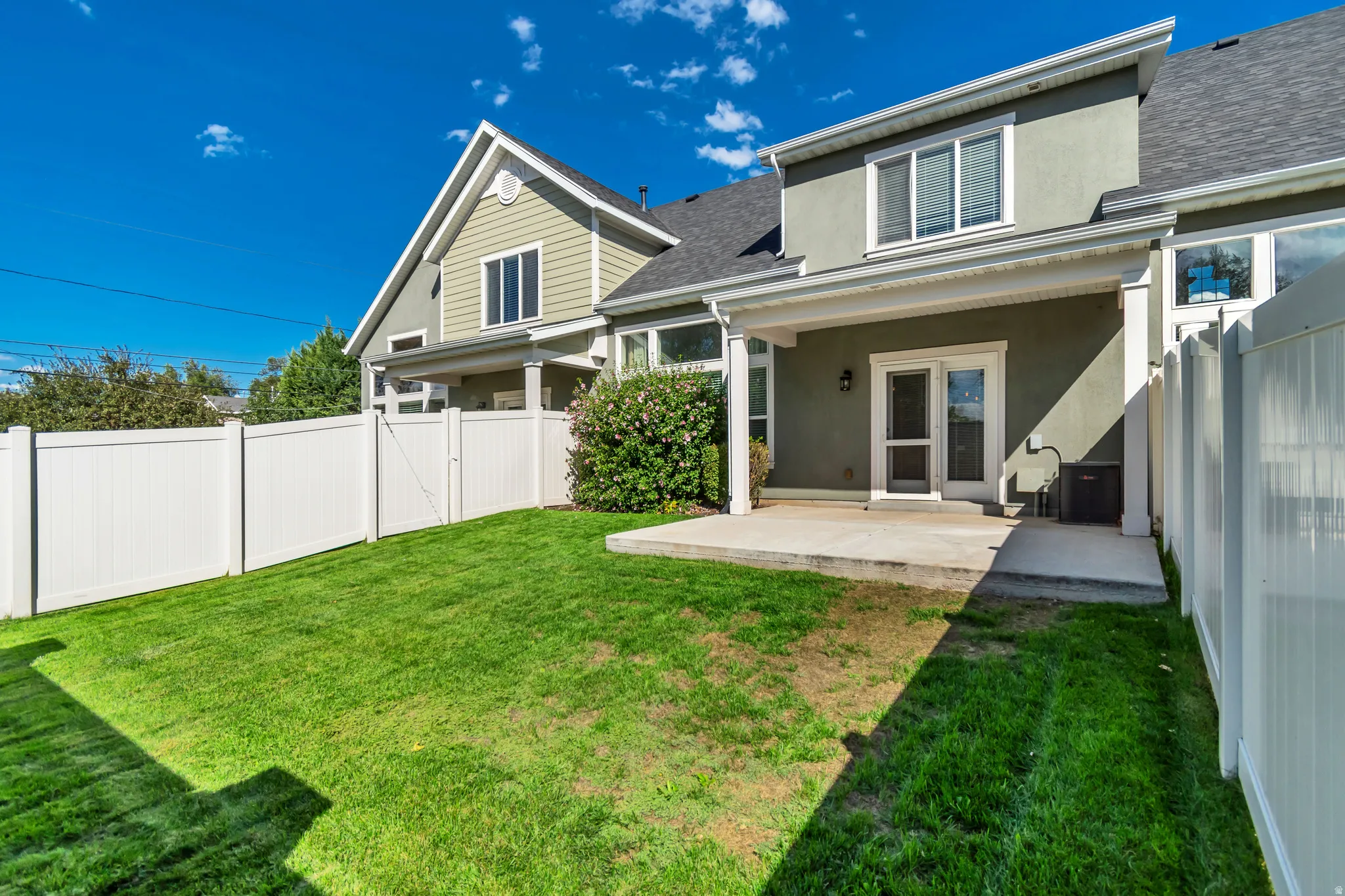Green lawn with white privacy fencing, a concrete patio, and a covered porch