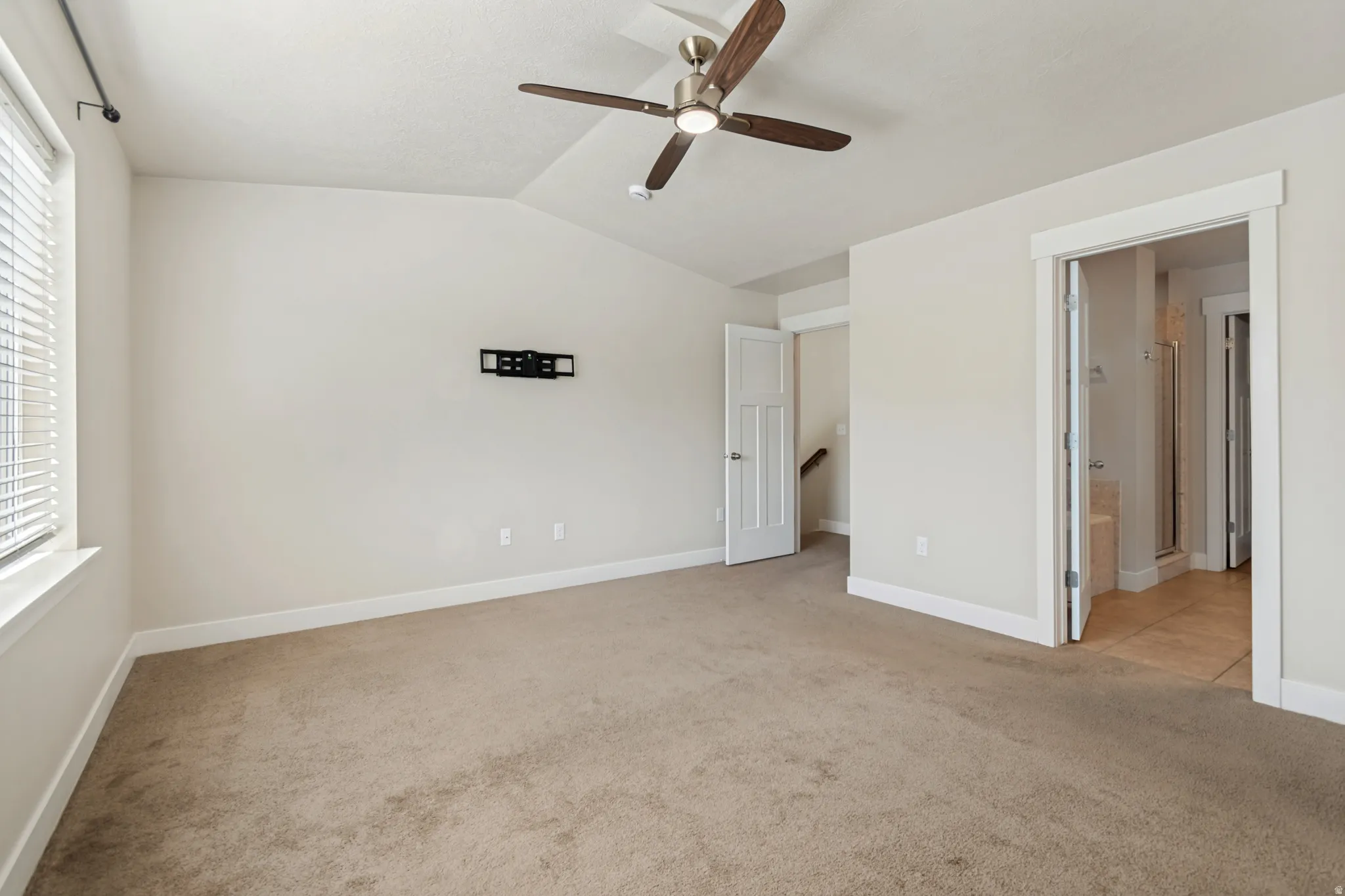 Sloped ceiling room featuring carpet flooring, a ceiling fan with light, and a wall-mounted television bracket