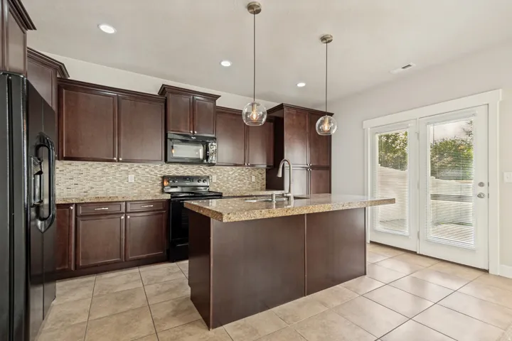 Kitchen featuring dark wood-finish cabinetry, a textured tile backsplash, a kitchen island with stone-finish countertops, and an integrated sink with a gooseneck faucet