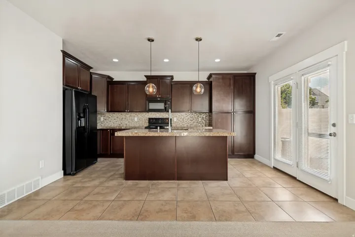 Kitchen featuring dark wood-finish cabinetry, a central island with a stone-finish countertop, black appliances, tile flooring, and double glass-paneled doors