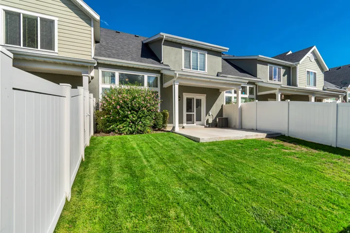 Expansive green lawn, white vinyl fencing, concrete patio, exterior access, and mature landscaping