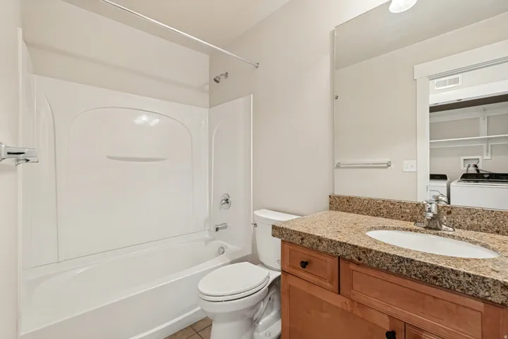 White tub and shower combination with chrome fixtures, wood-finish vanity with stone-finish countertop, and integrated sink