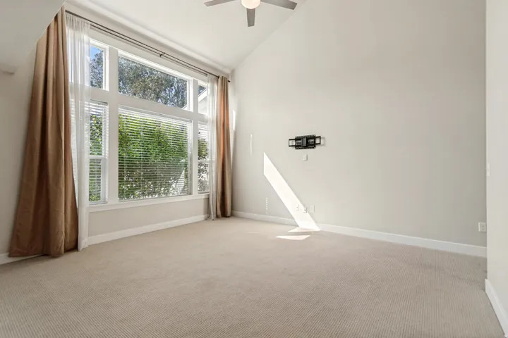 Vaulted ceilings, large windows, ceiling fan, and light-colored carpeting