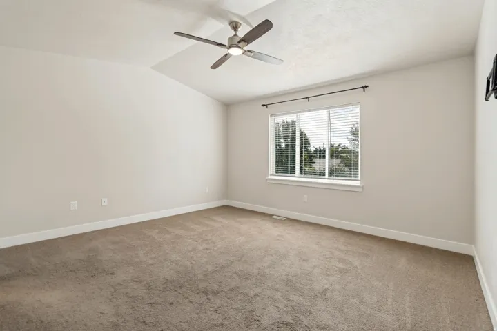 Vaulted ceiling with an attached ceiling fan, neutral wall finishes, large window with blinds, and carpeting