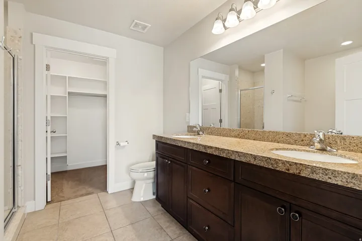 Dual vanity with integrated sinks, expansive mirror, light-toned countertop, dark wood-finish cabinetry, and tiled flooring