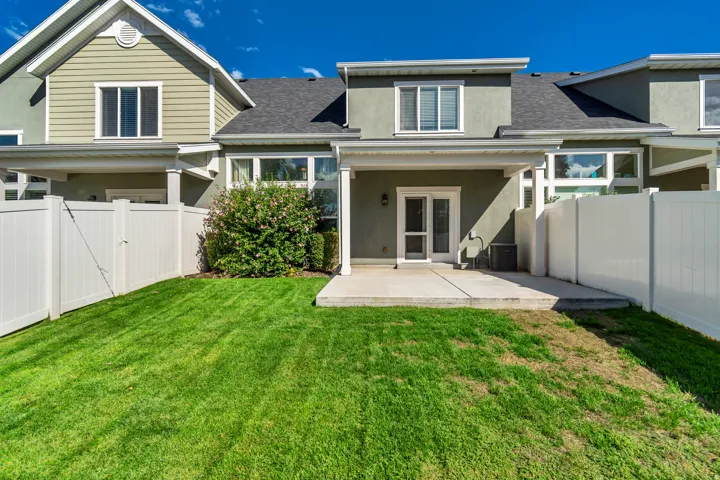 Expansive lawn area with a concrete patio, covered porch, and white privacy fencing