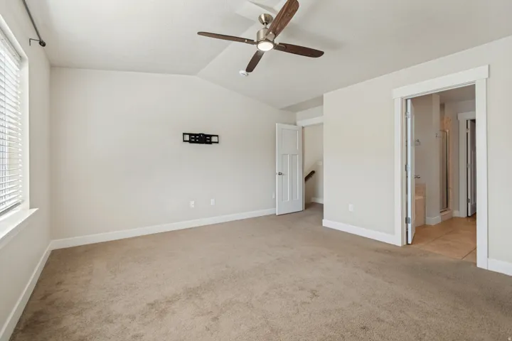 Sloped ceiling room featuring carpet flooring, a ceiling fan with light, and a wall-mounted television bracket
