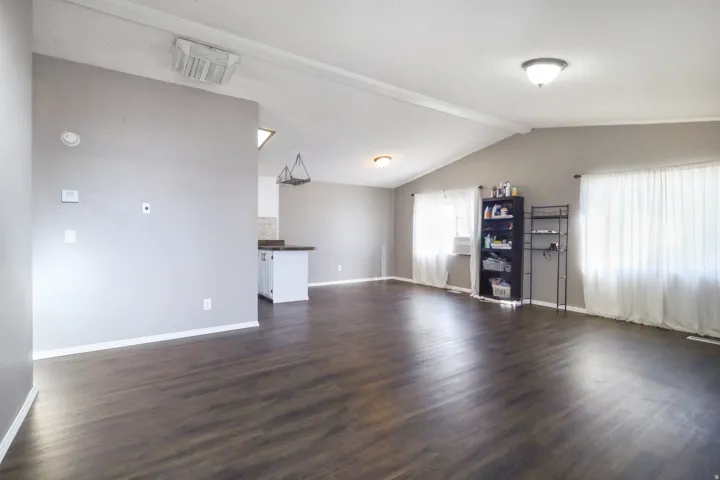 Spacious room featuring vaulted ceilings, dark wood-finish flooring, light grey painted walls, and recessed lighting