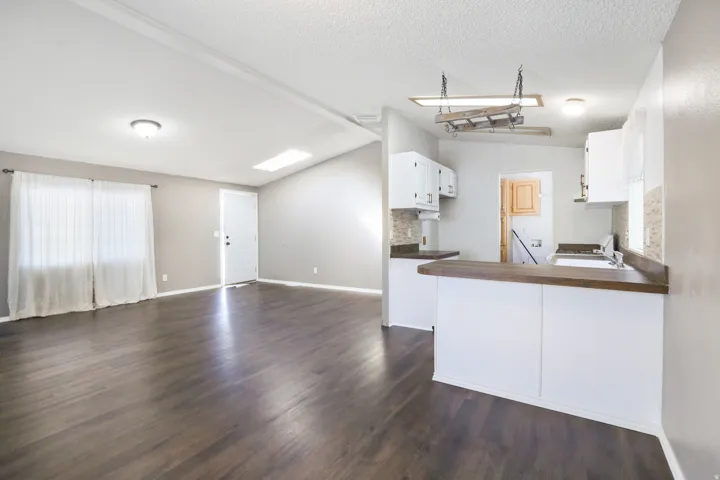 Wood-finish flooring throughout, vaulted ceiling with skylight, white cabinetry, wood-finish countertops, and tile backsplash