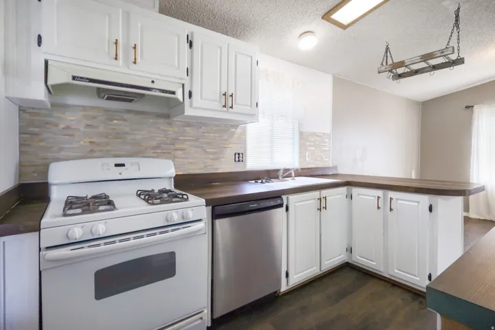 Kitchen featuring white cabinetry, dark wood-finish countertops, stainless steel dishwasher, white gas range, and a stacked stone-look backsplash