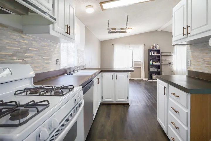 White cabinetry with bronze hardware, dark wood-finish countertops, tile backsplash, stainless steel dishwasher, and a white gas range