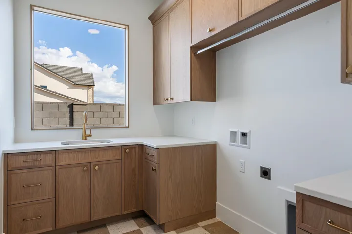 Wood-finish cabinetry, white countertops, built-in sink with a gold-tone faucet, and a large window
