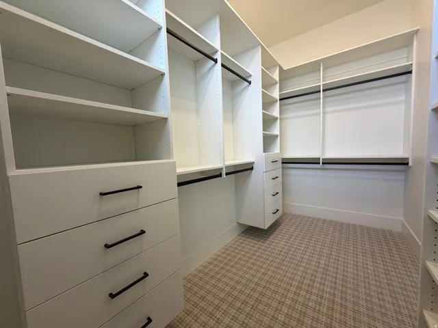 Built-in white cabinetry, multiple shelving units, integrated drawers with black hardware, black hanging rods, and patterned carpet flooring