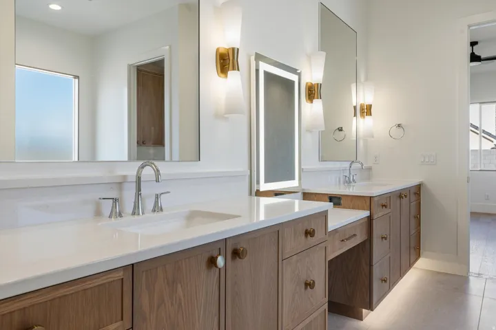 Double vanity with white countertops, wood-finish cabinetry, and contemporary wall sconces