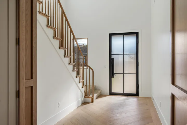 Entryway featuring a black-framed glass panel door, light wood-finish herringbone flooring, and a wood staircase with vertical balusters
