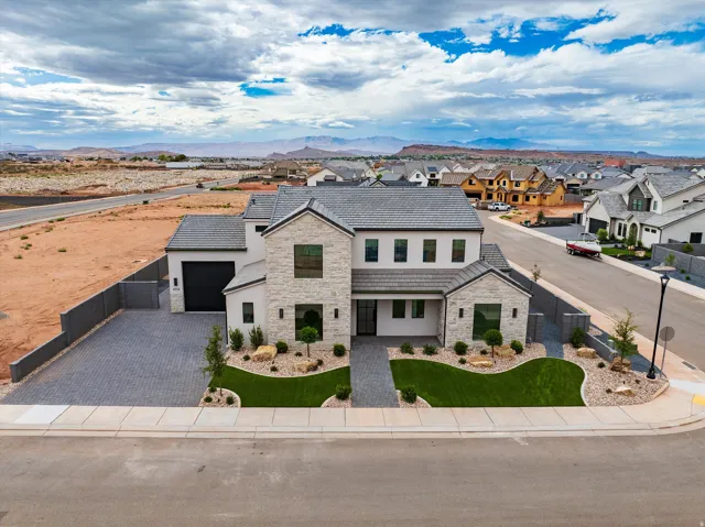 Stone and stucco exterior with a gray tile roof, paver driveway, and a manicured lawn with rock accents
