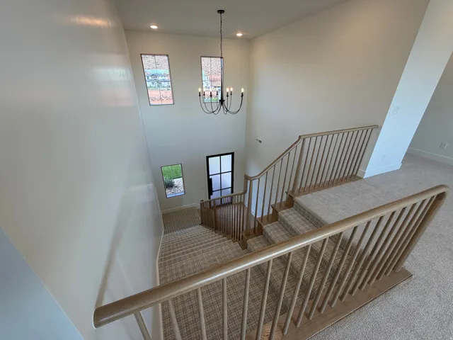 Two-story entry with a chandelier, upper-level windows, wood railings, and carpeted stairs