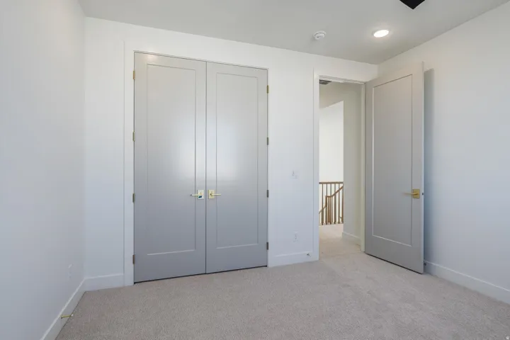 This bedroom has recessed ceiling lighting, light paneled doors with brass hardware, plush carpeting, and light walls