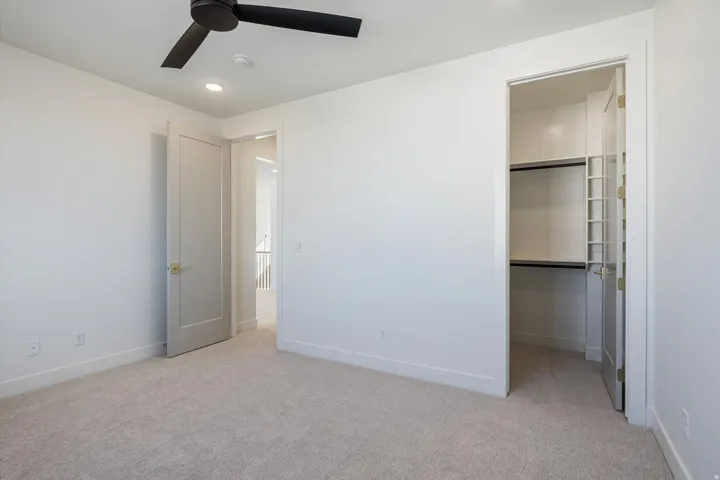 This bedroom has recessed ceiling lighting, ceiling fan, neutral carpeting, paneled interior doors, and a closet with built-in shelving