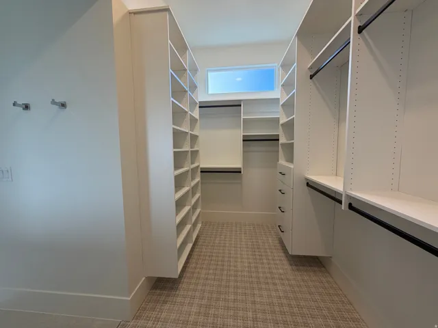 Custom-designed closet system with extensive shelving, built-in drawers, hanging rods, and a high-set window